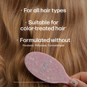 Pink hairbrush with text about hair product compatibility and ingredients on a close-up of brown hair.