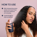 Woman with curly hair holding a bottle of hair product with usage instructions on a pink background