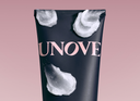 Close-up of a UNOVE product tube with creamy hair mask texture applied on the surface, set against a soft pink background