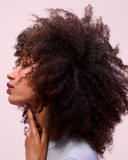 Side profile of a model with voluminous natural curls, highlighting textured hair against a soft pink studio background