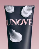 Close-up of a UNOVE product tube with creamy hair mask texture applied on the surface, set against a soft pink background
